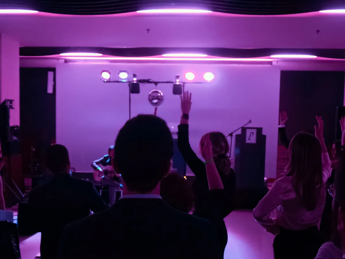 Asistentes con los brazos en alto ante el escenario, bajo luces violetas