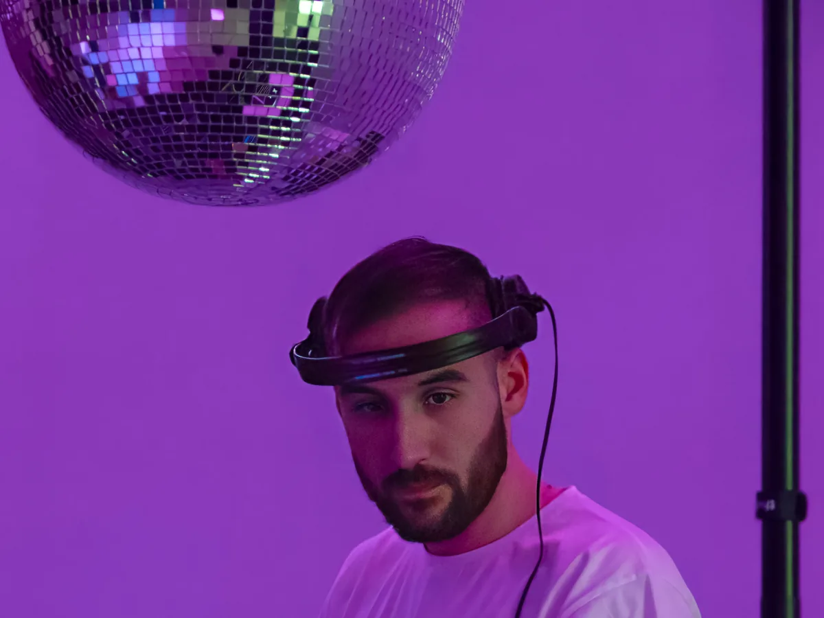 DJ con auriculares bajo la bola de espejos, con la luz violeta de la fiesta